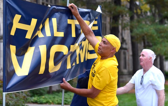 Anderson UM sexual-assault survivors Chuck Christian, left, and Jack Hanna, of Ann Arbor, a survivor from the 1979-1980 rowing team display a Hail To The Victims banner across the street from the UM President's house, Wednesday night, October 13, 2021, before a protest.