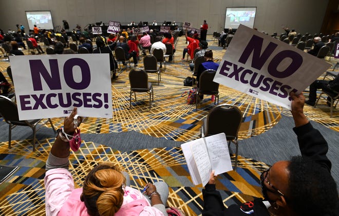 Friends Denise Robinson, left, of Southfield, and Loretta Hobbs, of Detroit, hold up signs during public comments, Wednesday afternoon, October 20, 2021.