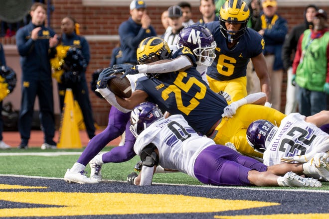 Michigan running back Hassan Haskins stretches over the top of Northwestern ' s Cole Freeman to score a touchdown during the third quarter.