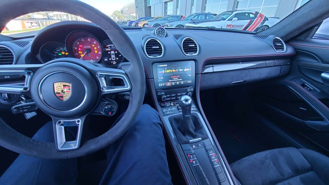 The cockpit of the 2021 Porsche Cayman GTS, including Sport Mode button on the steering wheel, manual shifter and console sleeve of control buttons.