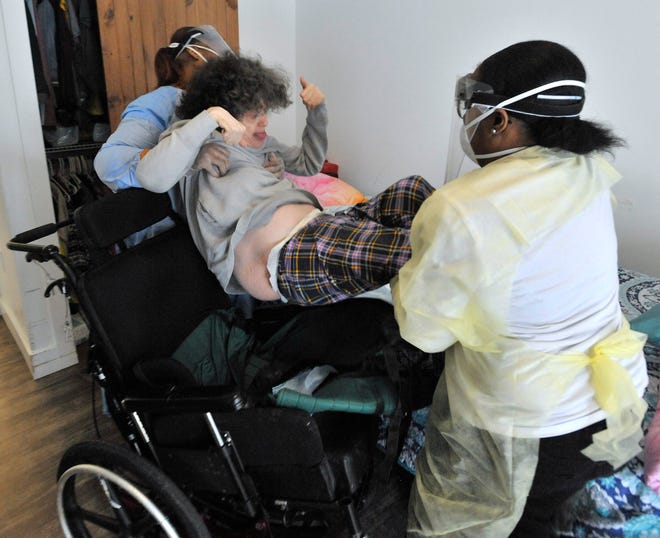 Residential supervisor Tracy Kroll (not pictured) stands at the ready as resident-support-staff workers Sequoia Armstrong, left, and Africa Sydnor, right, lift resident Jan Parker into bed for a nap after lunch, Wed. Jan. 19, 2022.