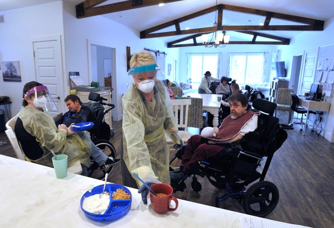 Pioneer Resources CEO Jill Bonthuis, center, grabs a cup for resident Gerald Christensen, right, 
as residential supervisor Tracy Kroll, left, feeds Mary Miller, Wed. Jan. 19, 2022.