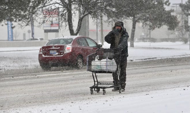 A man pushes a shopping cart along 8 Mile Road near I-75 in Detroit as sidewalks become impassable due to heavy snowfall on Monday.