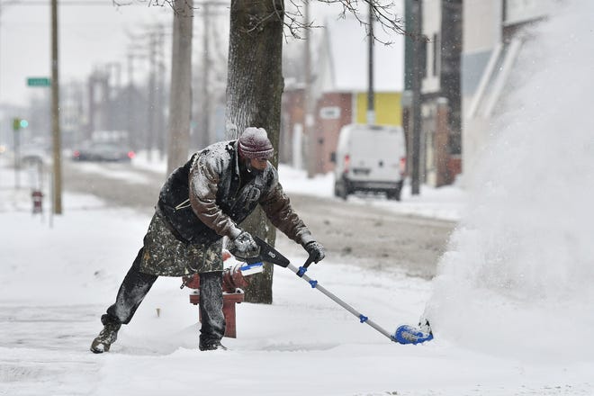 Sylvester Robinson, 57, of Detroit uses an electric snow blower to clear snow on Horton Street during a snowfall in Detroit on Jan. 24, 2022.