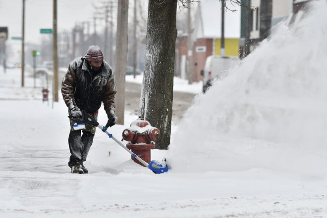Sylvester Robinson, 57, of Detroit uses an electric snow blower to clear snow on Horton Street during a snowfall in Detroit on Jan. 24, 2022.