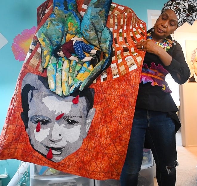 Artist April Anue Shipp holds a piece of fabric art that represents the story of a 3-year old Serian refugee named Alan Kurdi who died, along with his mother and brother, when the boat they were on capsized and eventually his body washed a shore in Turkey in 2015.