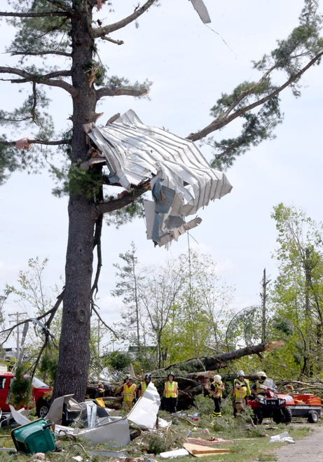 Rescue workers stand under a tree, which has parts of a mobile home stuck in the branches on Saturday, May 21, 2022.
