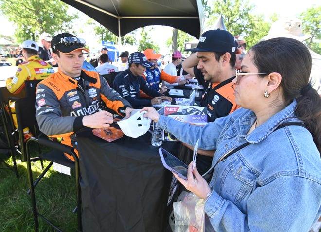 Indy driver Pato O'Ward (left) signs an autograph for race fans Mario Gonzalez and Daniela Sanchez during the 2022 Chevrolet Detroit Grand Prix on Saturday, June 4, 2022.