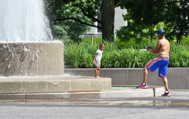 Emerson Clark, 60, of Detroit takes a photo as he lets his daughter Legacy, 3, cool down a little in one of the fountains in front of the Detroit Institute of Arts in Detroit on June 15, 2022.