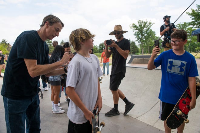 Legendary skateboarder Tony Hawk autographs the t-shirt of young skater Mason Farley, left, while his friend Cullen Messing, takes a picture on his phone. Both boys are 13 and from Macomb Township.