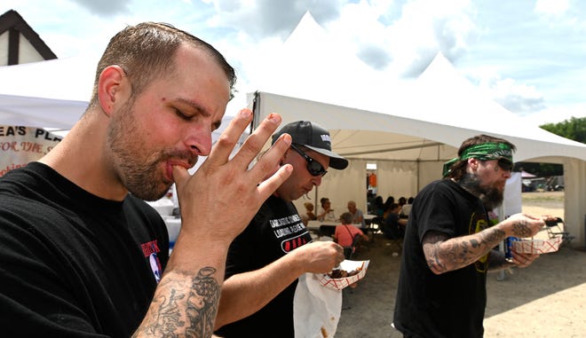 Friends and Davisburg residents Garret Tripp, left, Richard Bowlby, a.k.a. "Rampage Asylum," and Kevin Masten eat ribs from Cowboys Barbeque & Rib Co., Saturday afternoon, July 2, 2022. Cowboys is out of Fort Worth, Texas. Bowlby is a freak show performer.