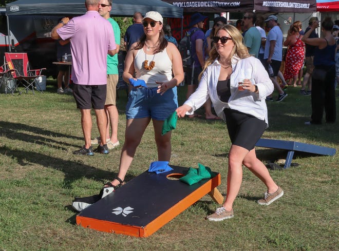 Maddie Davis, of Ann Arbor, looks on as Heather Dangel, of Livonia, tosses a cornhole bag at the New Holland Brewing area at the Michigan Brewers Guild Summer Beer Festival Friday in Ypsilanti's Riverside Park. Dangel doesn't spill a drop.