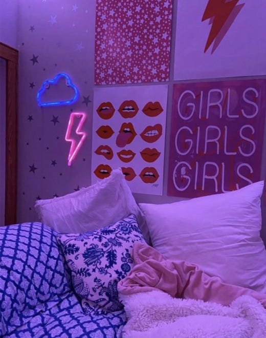 A colorful mix of neon signs and other graphic artwork create a collage effect above the bed. Fun additions like these can make a dorm room feel lived in.