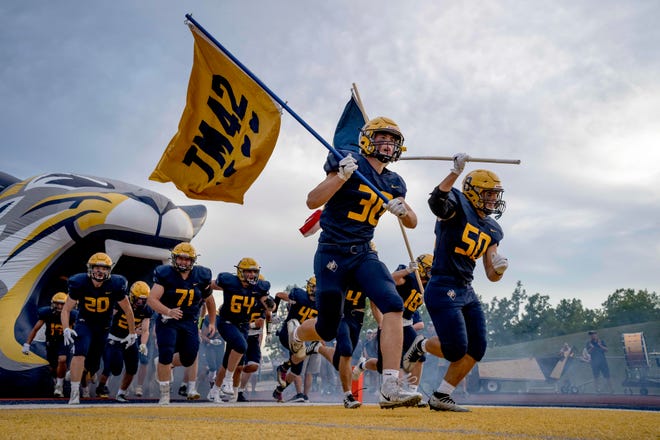 Oxford senior Logan Wilmot (30) takes the field while holding a flag in memory of Tate Myre before the high school football game between the Oxford Wildcats and Birmingham Groves Falcons at Oxford High School in Oxford, Mich. on Sept. 2, 2022. (Nic Antaya, Special to The Detroit News)