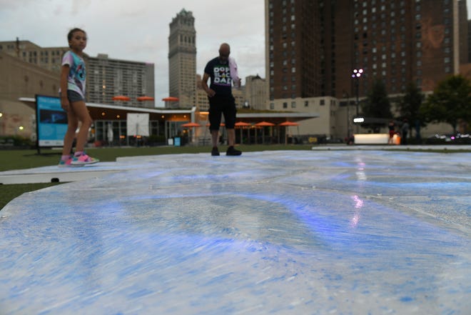 From left, Aliyana Stokes, 8, and her father Aaron Stokes, 55, of Berkley walk on The Last Ocean art installation at Beacon Park in Detroit on Sept. 21, 2022.  The blue in the plastic panels is from bottle caps, the white from yogurt containers and milk jugs, and the translucent is from water bottles, all reclaimed ocean plastic.  The work will be at Beacon Park through Sept. 26.