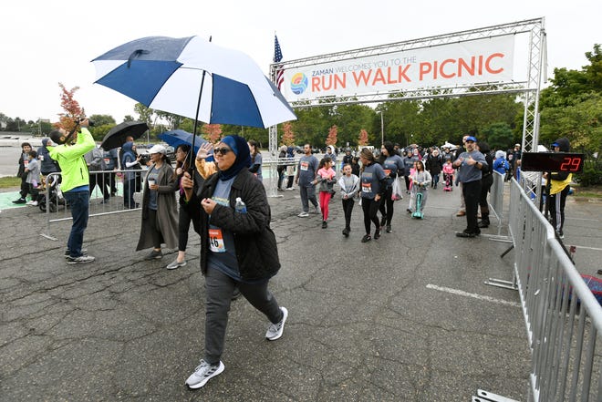 Walkers, some carrying umbrellas to protect themselves from the rain, take part in a 5K Walk during the Zaman International 13th annual Run Walk Picnic at Ford Field Park, Saturday, Sept. 24, 2022, in Dearborn, Mich. (Jose Juarez/Special to Detroit News)