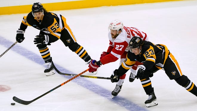 Red Wings' Austin Czarnik (27) pushes the puck up ice between Penguins' Brock McGinn (23) and Teddy Blueger (53) during the first period.