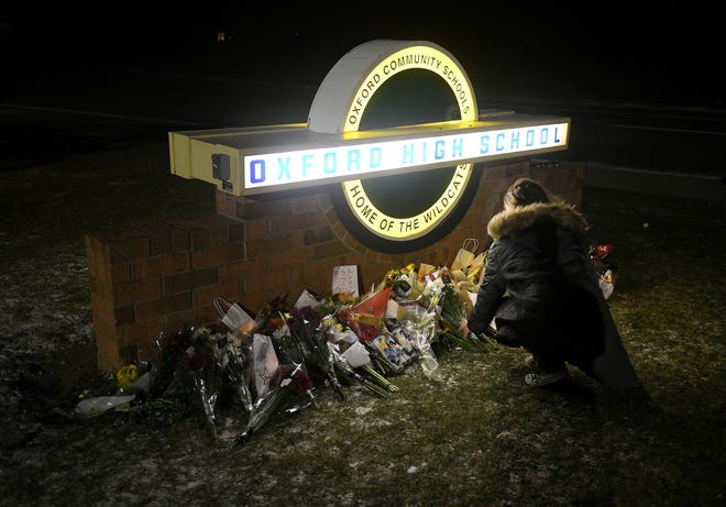 An unidentified youth adds to the flowers, candles and other items placed under the sign at Oxford High School in Oxford, Mich. on Nov. 30, 2022.