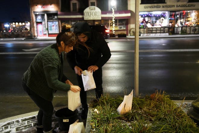 From left, Marcela Chisaca of Auburn Hills and manager at Casa Real restaurant and Diego Fajardo put dirt in the bottom of the bagged luminaries to put in front of the restaurant in Oxford, Mich. on Nov. 30, 2022.  Luminaries are lit and on display in Oxford in memory of the four students killed one year ago at Oxford High School.