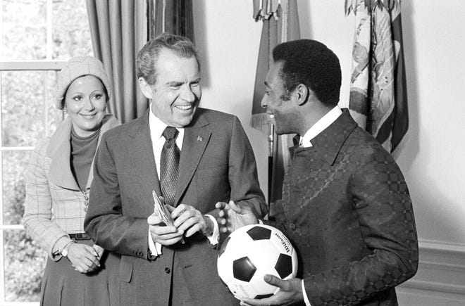 In this May 8, 1973 file photo, Brazil's soccer player Pele holds a ball he autographed for U.S. President Richard Nixon, who holds a 1957 newspaper clipping shown them together in Sao Paolo, Brazil, and Pele's wife Rosemeri dos Reis Cholbi looks on, at the chief executive's office in Washington, D.C.