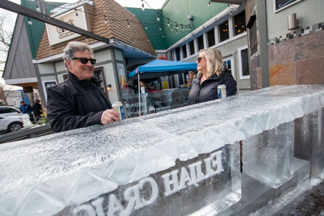 Joe Spoto of West Bloomfield Township and his wife, Jennifer, enjoy an adult beverage at a bar made from ice in front of E.G. Nicks restaurant during the Plymouth Ice Festival, in Plymouth, February 5, 2023.
